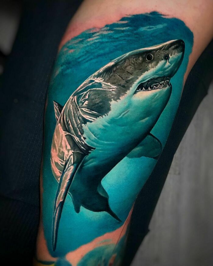 A super realistic tattoo of a great white shark in vivid ocean colors on a person’s arm.