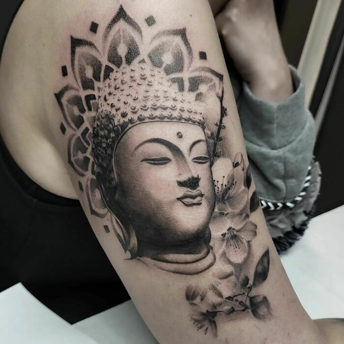 Realistic tattoo of a serene Buddha face with floral elements on the arm, showcasing detailed artistry.
