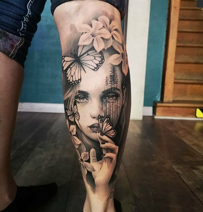Realistic tattoo on leg depicting a woman's face with butterflies and flowers in a highly detailed design.