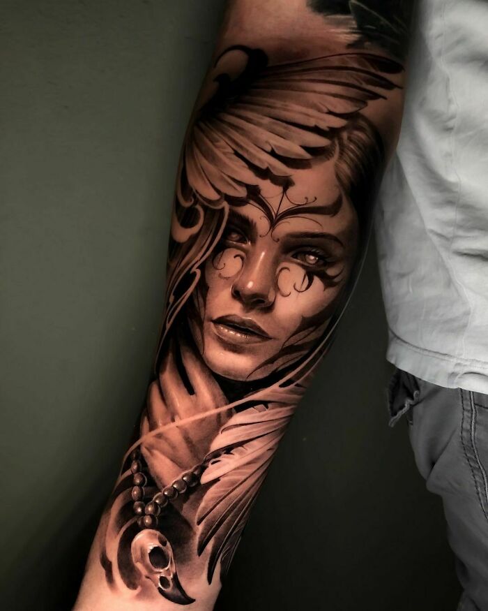 Realistic tattoo of a woman's face with wings and detailed shading on forearm.