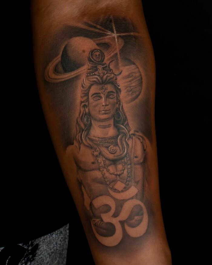 Realistic tattoo of Shiva with cosmic elements on forearm, featuring intricate details and shading.