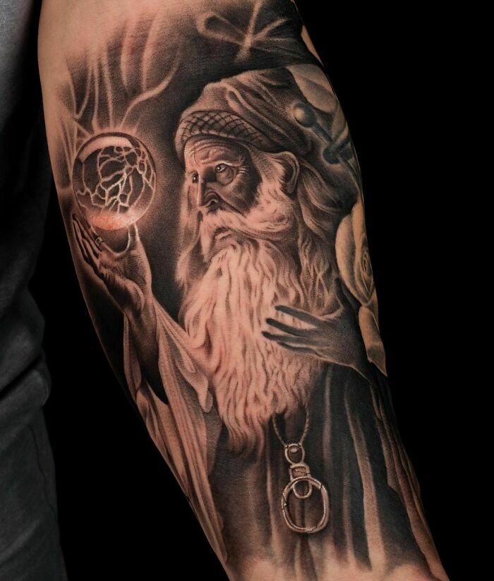 Realistic tattoo of an elderly sage holding a glowing orb, intricately detailed on the arm.