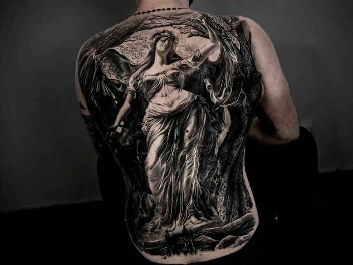 Realistic tattoo of a detailed angel on a person's back, showcasing intricate and flawless artistry.