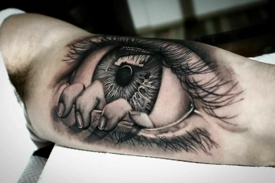 Realistic tattoo of an eye with hand fingers emerging, detailed art on arm.