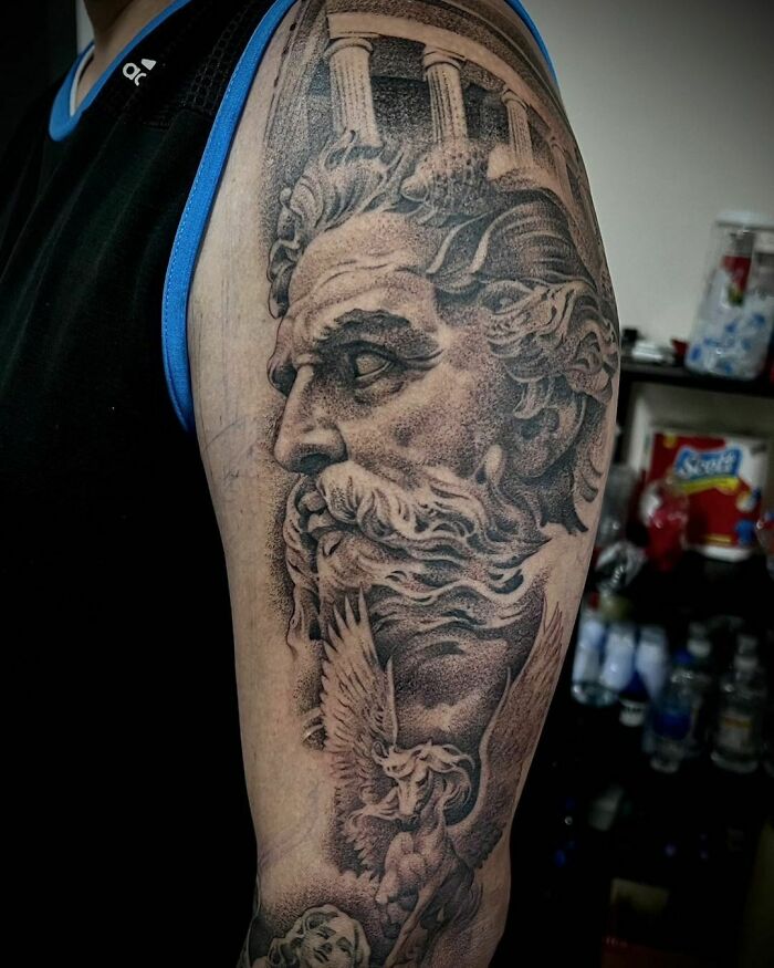 Realistic tattoo of a Greek god with detailed architecture on a person's arm, showcasing flawless artistic skill.