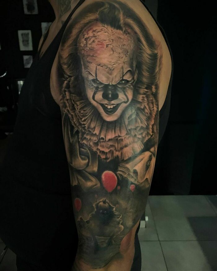 Realistic tattoo of a horror clown on an arm, showcasing intricate details and shadows.