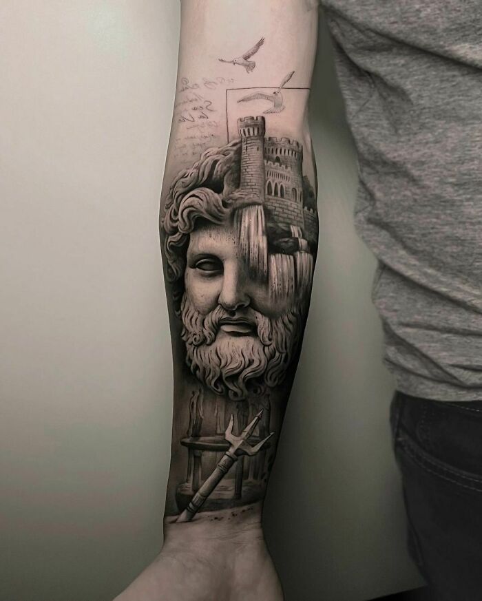 Realistic tattoo of a bearded statue with a castle and trident on a person's forearm.