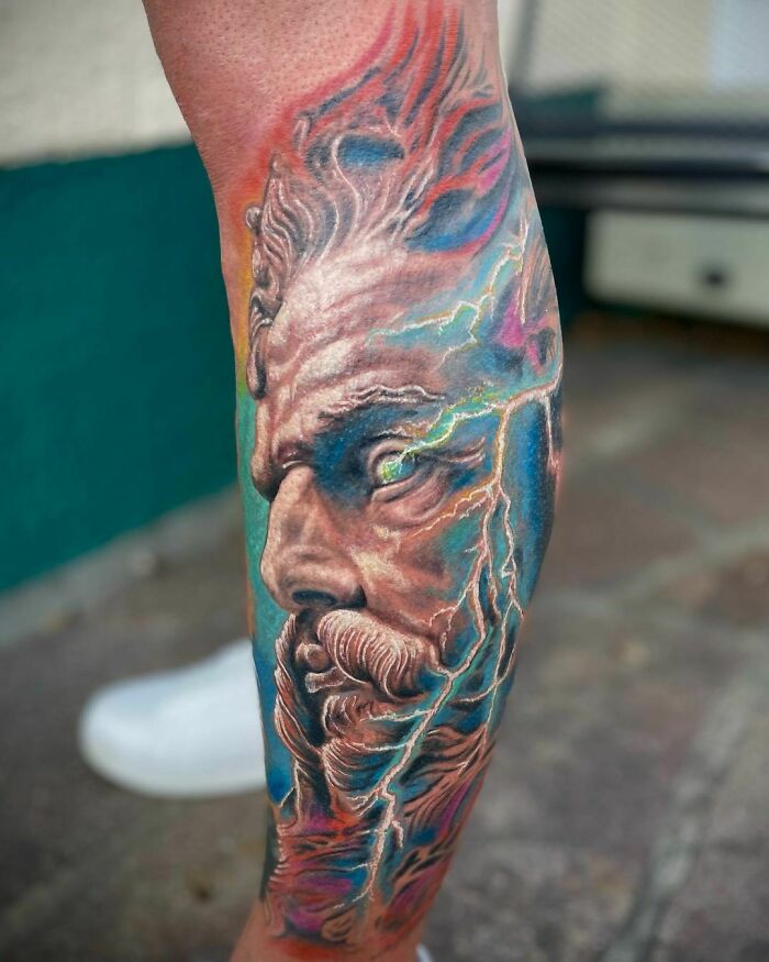 Realistic tattoo of a detailed face with vibrant colors and intricate patterns on a person's calf.