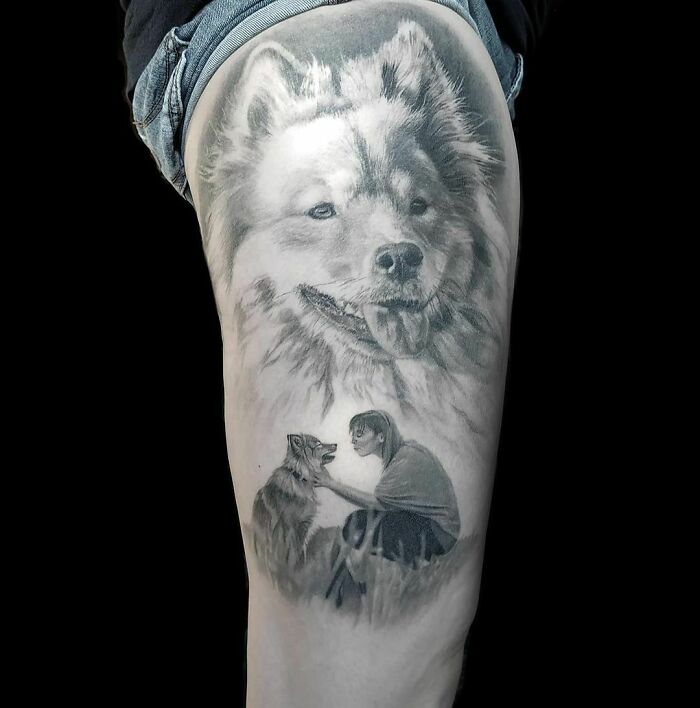 Realistic tattoo of a dog and a person kneeling, seen on an upper thigh.