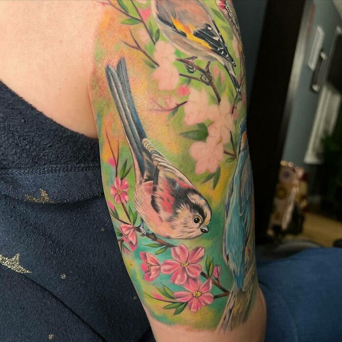 Realistic tattoo of birds and flowers on an arm, showcasing flawless artistic detail and vibrant colors.