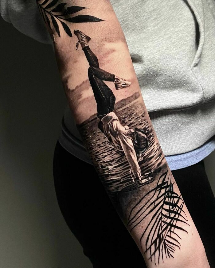 Realistic tattoo on a forearm depicting an inverted figure by water, accented by leaf designs.