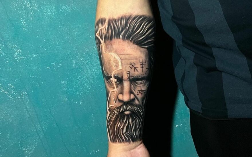 Realistic tattoo on a forearm, featuring a detailed face with symbols and lightning effects.