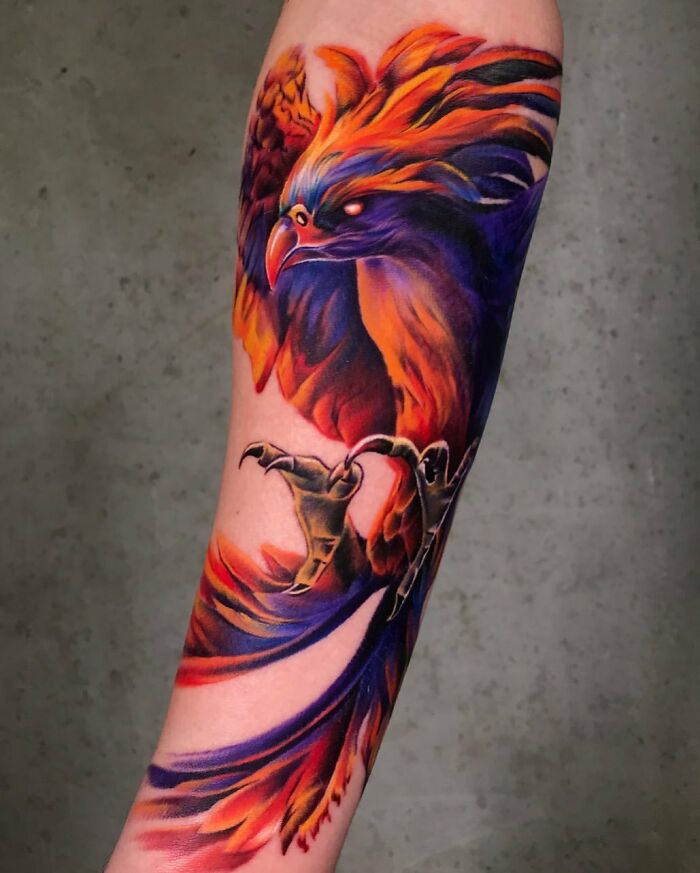 Colorful realistic tattoo of a phoenix on an arm, showcasing vibrant red, orange, and purple feathers.
