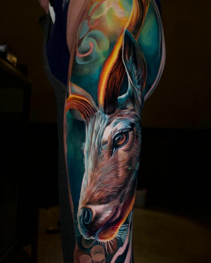 Realistic tattoo of a colorful deer head on an arm, showcasing vibrant detail and artistic flair.