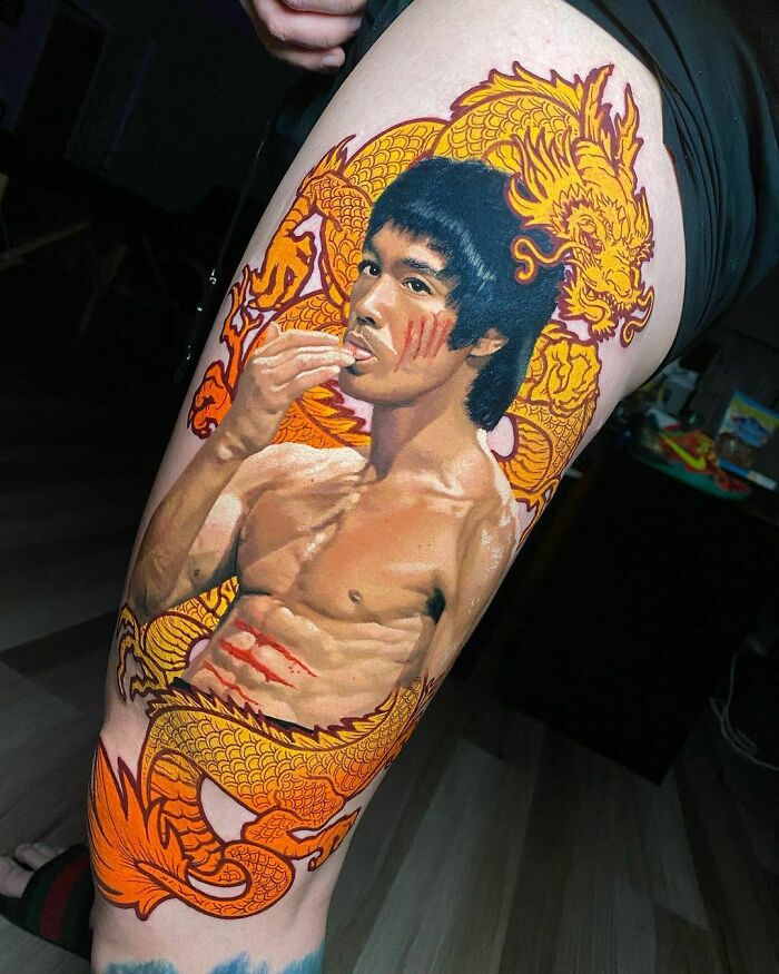Realistic tattoo of a shirtless man with dragon design on a person's leg, showcasing detailed art and vivid colors.