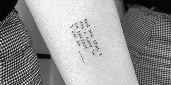 Close-up of a creative word tattoo on an arm, featuring an inspirational quote in black ink.