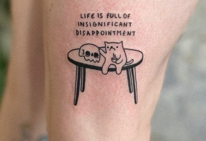 Tattoo of a cat and a skull on a table with text about life's insignificant disappointments.