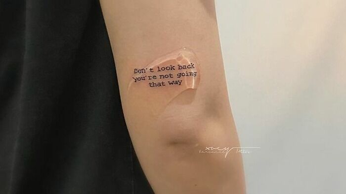 Arm with "Don't look back" word tattoo under a clear bandage, showcasing creative word tattoo design.