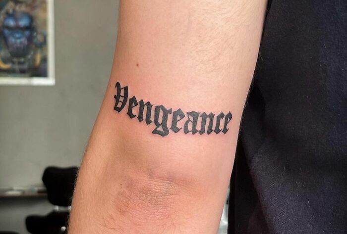 "Creative word tattoo reading 'Vengeance' on a person's arm in bold black letters."