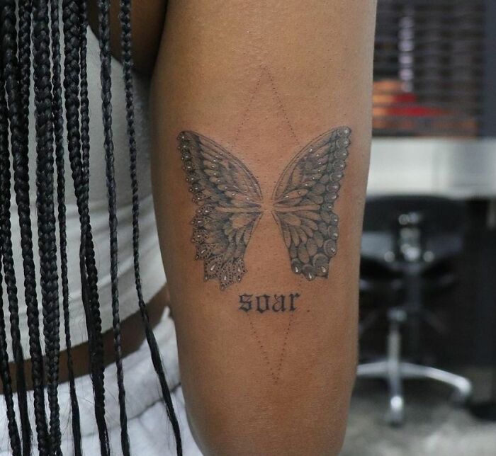 Butterfly wing tattoo with the word "soar" on an arm, showcasing creative word tattoo inspiration.