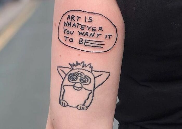 Creative word tattoo with phrase "Art is whatever you want it to be" alongside a cartoon creature.