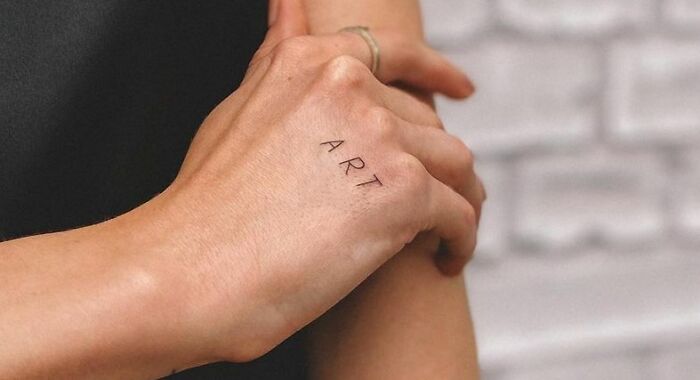 "Minimal word tattoo reading 'ART' on a person's hand for creative inkspiration."