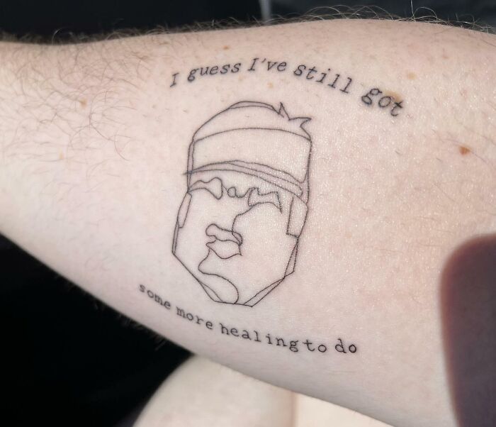 Line art tattoo with text "I guess I've still got some more healing to do" on arm; creative word tattoos.