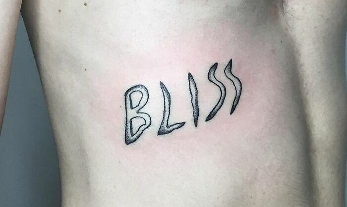 "Word tattoo 'BLISS' in unique font on a person's side, showcasing creative tattoo ideas."
