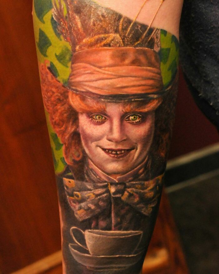 Super realistic tattoo of a character with vibrant red hair, top hat, and a green background on a forearm.