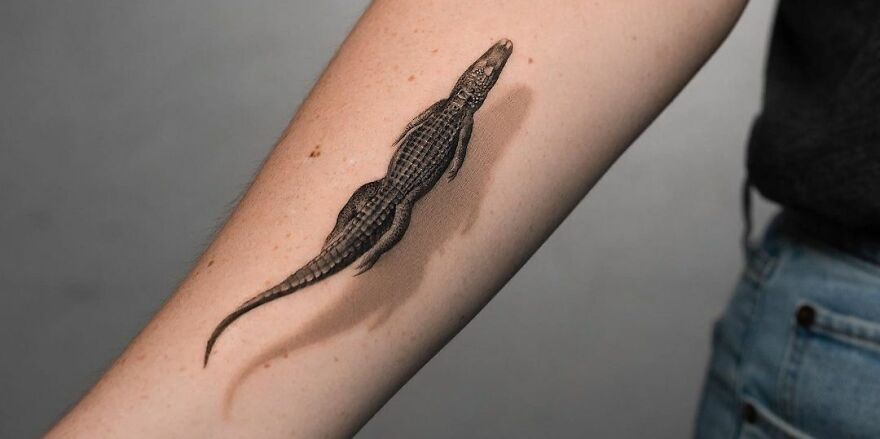 Realistic tattoo of a crocodile on a person's forearm, showcasing detailed art.