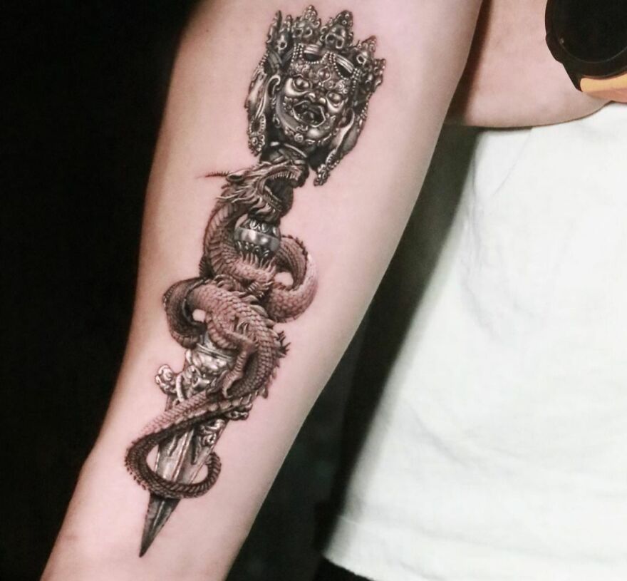 Realistic tattoo of a detailed dragon entwined with a dagger on a person's forearm.