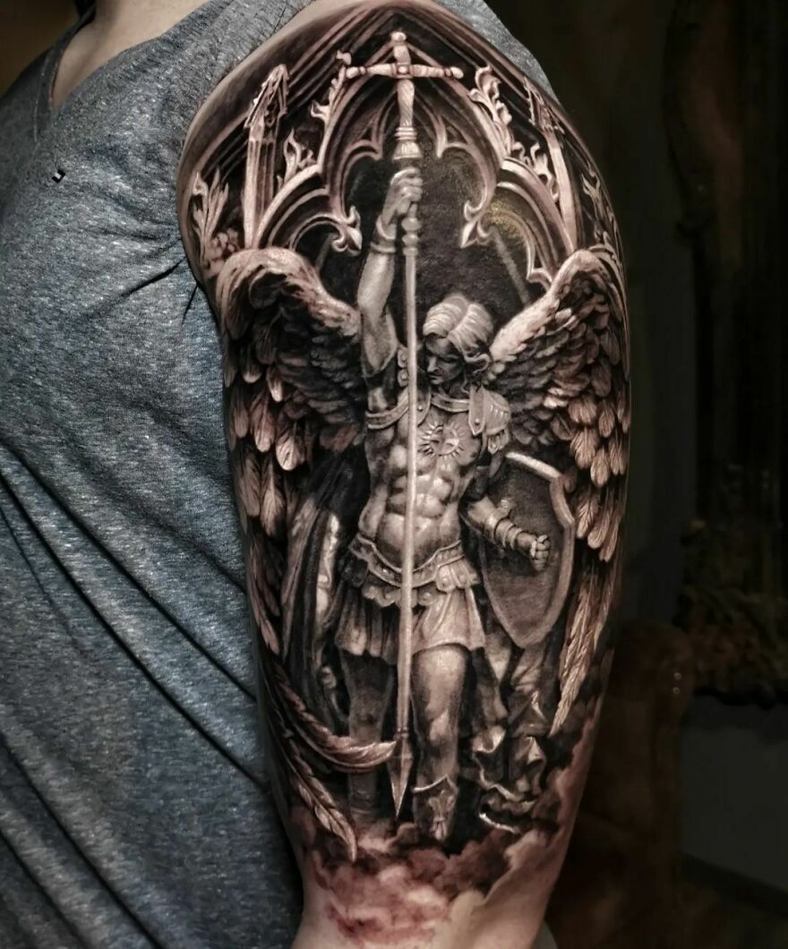 Realistic tattoo of an angel statue with a sword, showcasing intricate detailing on the shoulder.