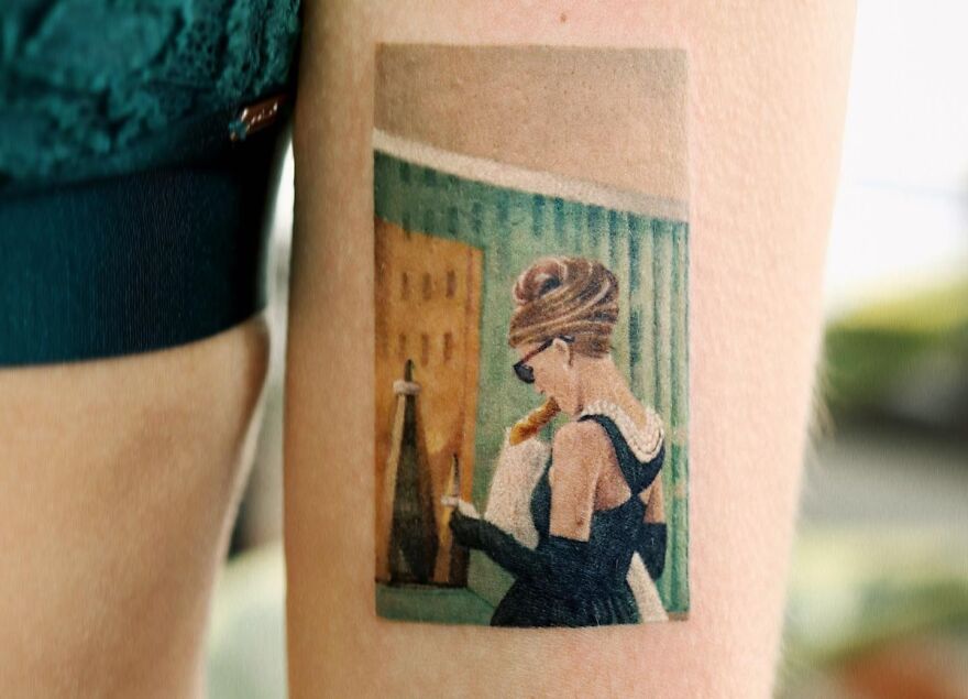 Realistic tattoo of iconic movie scene in vibrant colors, featuring a stylish woman with a city backdrop.