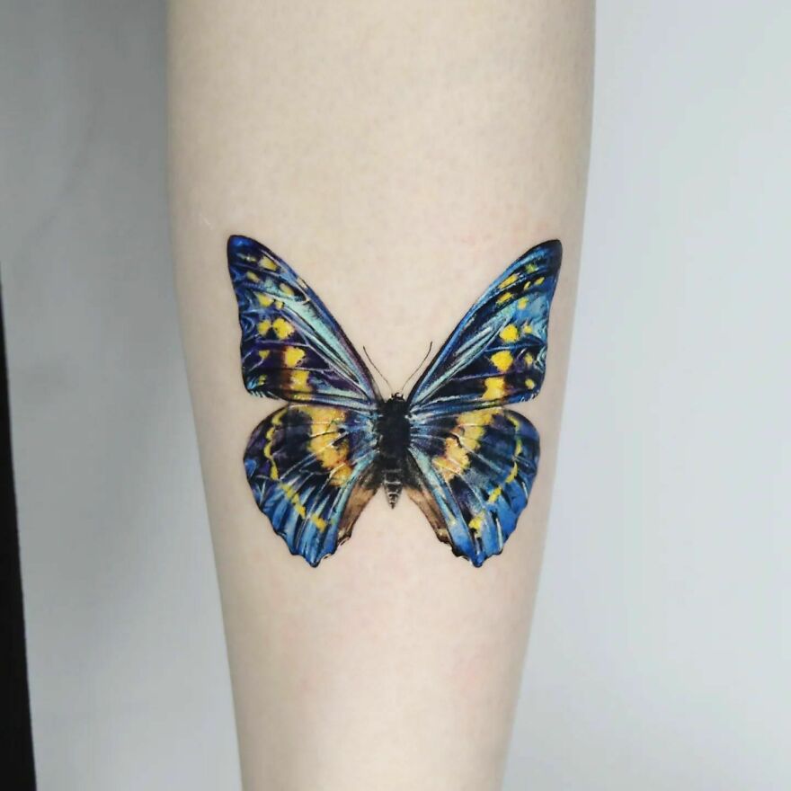 Blue and yellow butterfly tattoo showcasing realistic detailing on skin.
