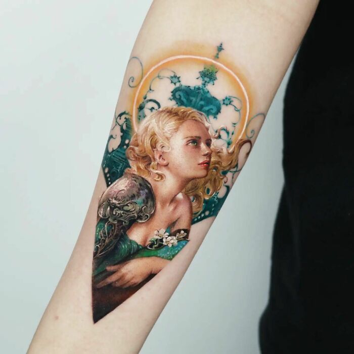 Realistic tattoo of a woman with blonde hair, adorned in intricate designs on a forearm.