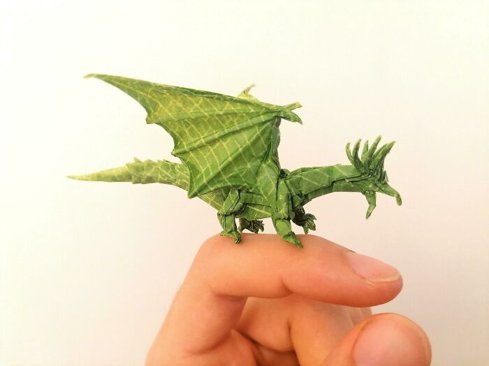 a green paper dragon sitting on the finger