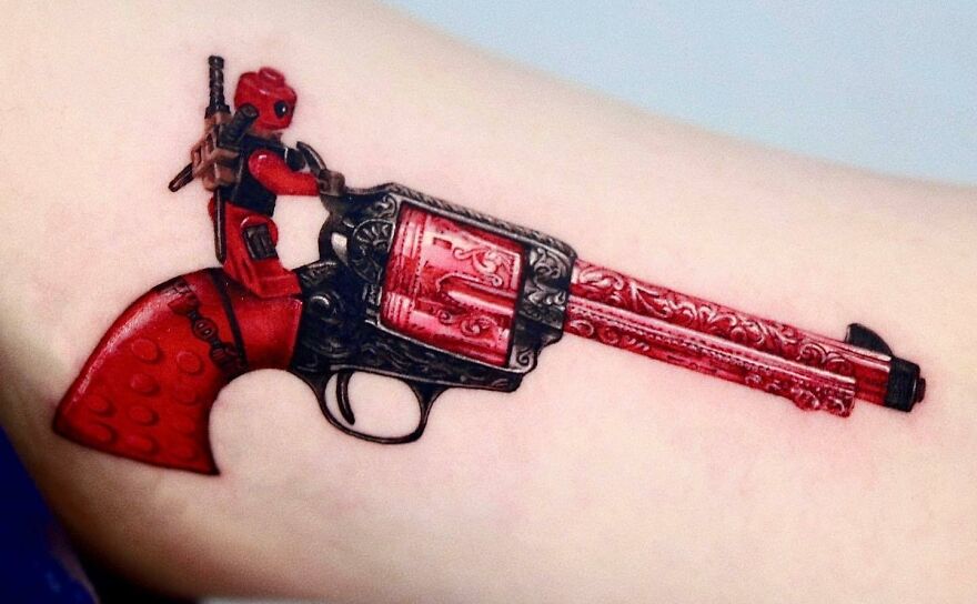 Super realistic tattoo of a detailed, red-themed revolver with a character sitting on top.