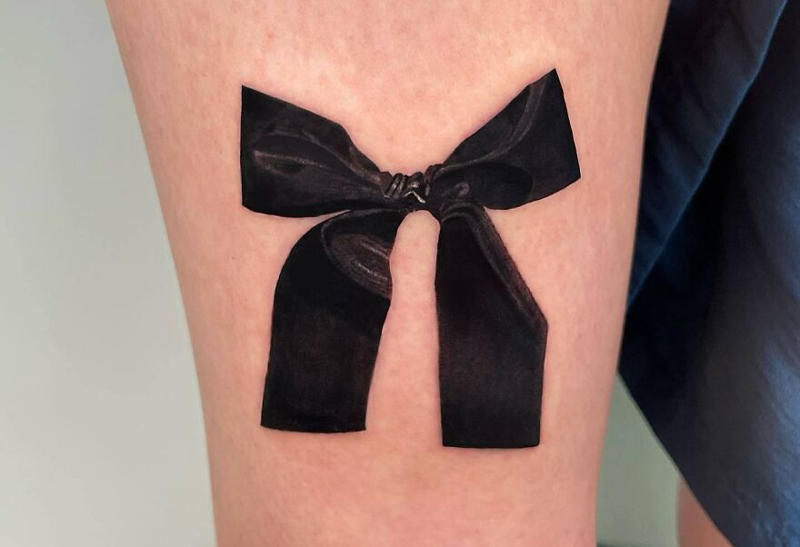 Realistic tattoo of a black bow on skin, showcasing detailed artistry and shading techniques.