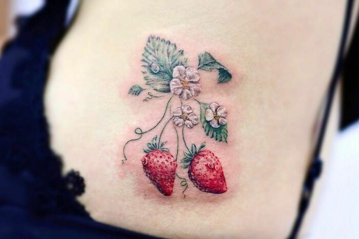 Realistic tattoo featuring detailed strawberries and floral elements on skin.