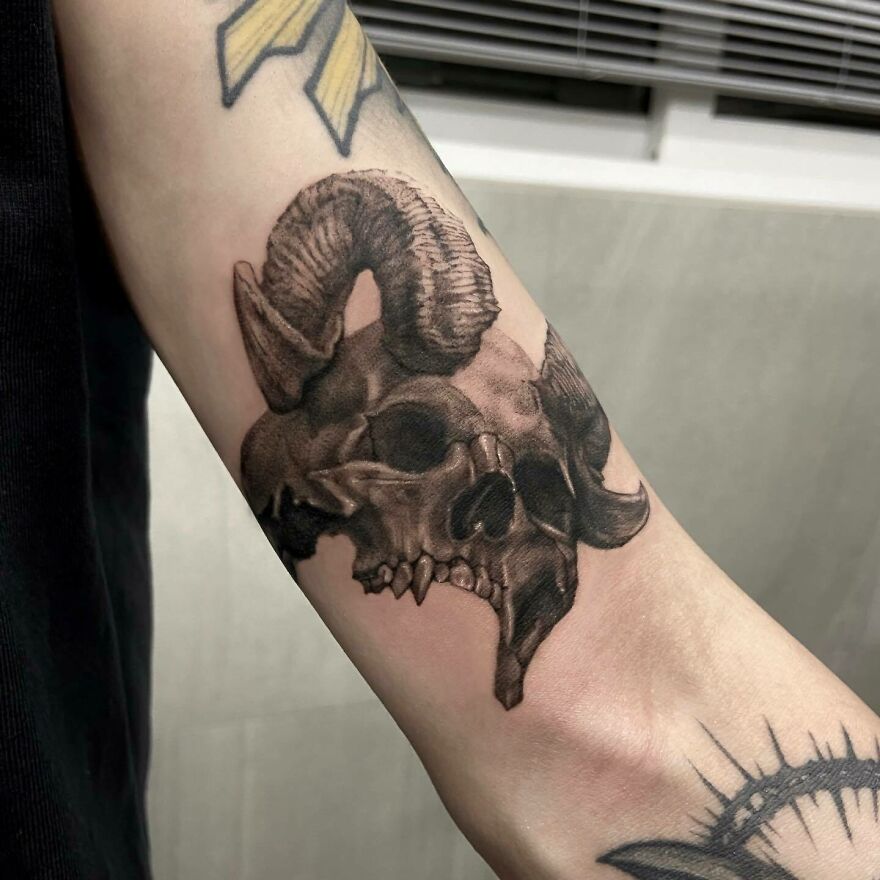 Realistic skull with horns tattoo showcasing intricate detailing on the arm.