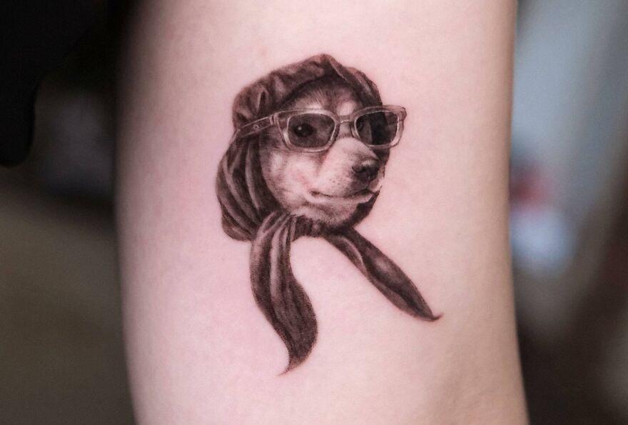 Realistic tattoo of a dog wearing sunglasses and a scarf on skin.