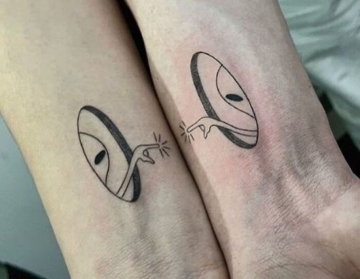 Matching tattoos on wrists featuring two hands reaching out from portals.