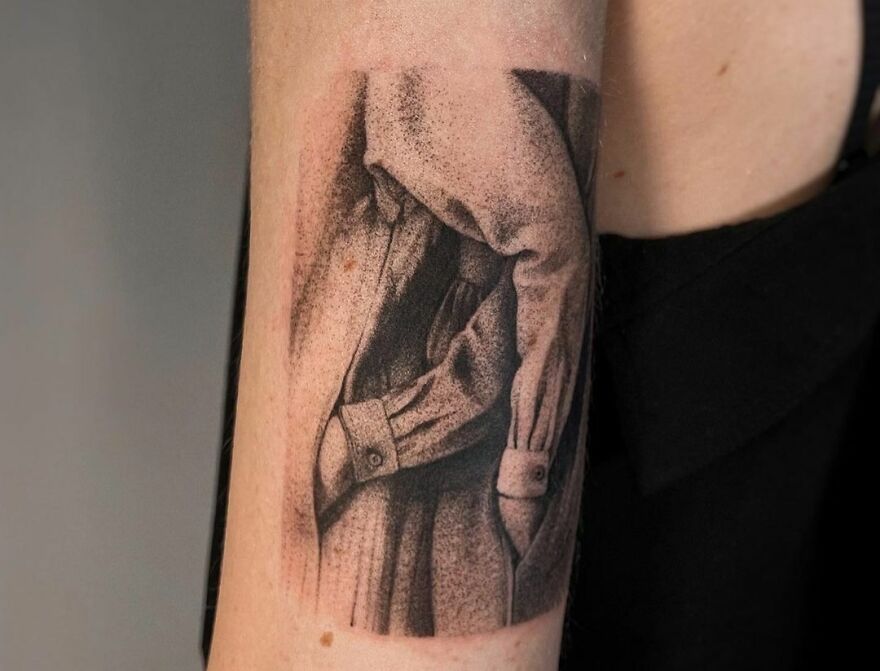 Realistic tattoo of a draped cloth shirt on an arm, showcasing intricate details and shading.
