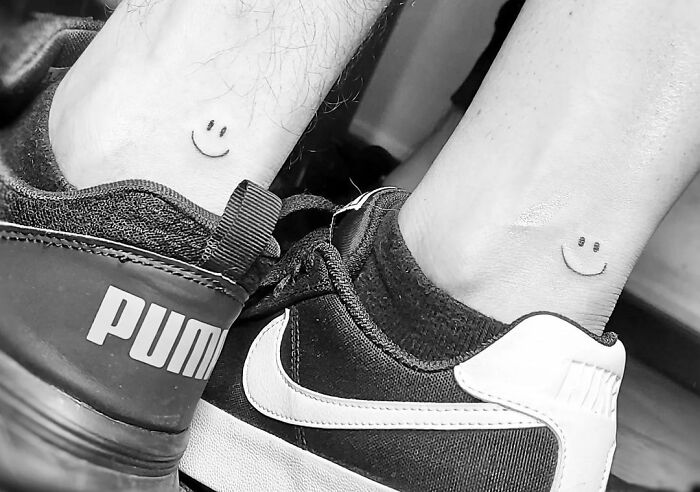 Matching tattoos on ankles with smiley faces, next to Puma and Nike sneakers.
