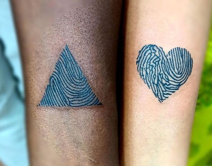 Matching tattoos of a triangle and heart with fingerprint patterns on two arms.