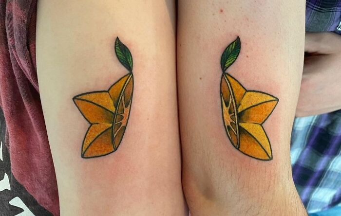 Matching tattoos of orange slices with green leaves on two arms.