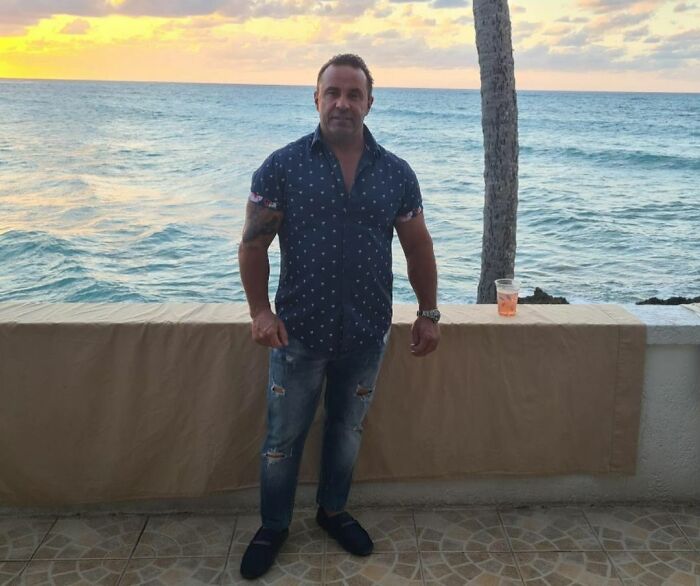 A man in a blue shirt standing by the ocean at sunset, related to celebrities who went to jail.