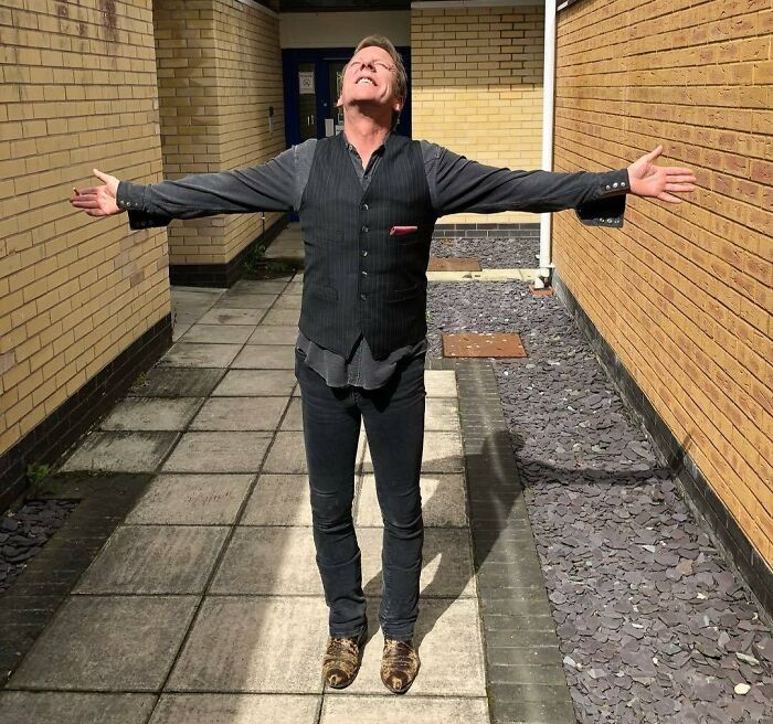 Celebrity standing with arms outstretched in a brick courtyard, expressing a sense of freedom.