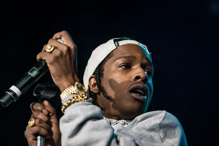Celebrity performing on stage, wearing a cap and jewelry.