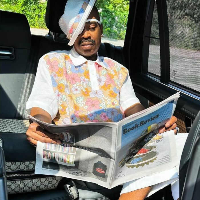 A celebrity wearing a floral shirt reads a newspaper in a car, highlighting their past involvement with the law.